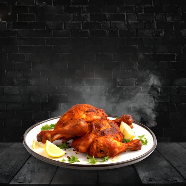 Steaming Indian tandoori chicken with lemon wedges and cilantro on a white plate.