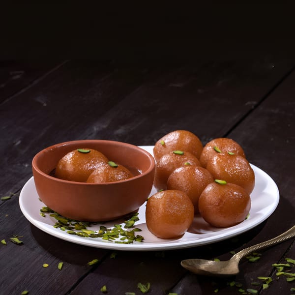 Gulab Jamun, an Indian dessert, in a terracotta bowl and on a white plate with pistachio garnish.