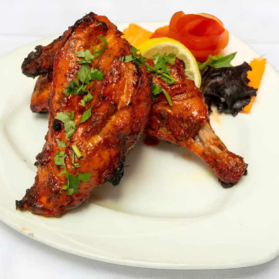 Manhattan Valley Indian Restaurant's Tandoori Chicken, garnished with cilantro, lemon, and carved vegetables.