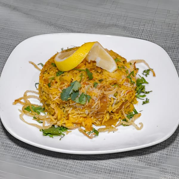 Indian biryani with rice, cilantro, fried onions, and lemon wedges on a white plate.