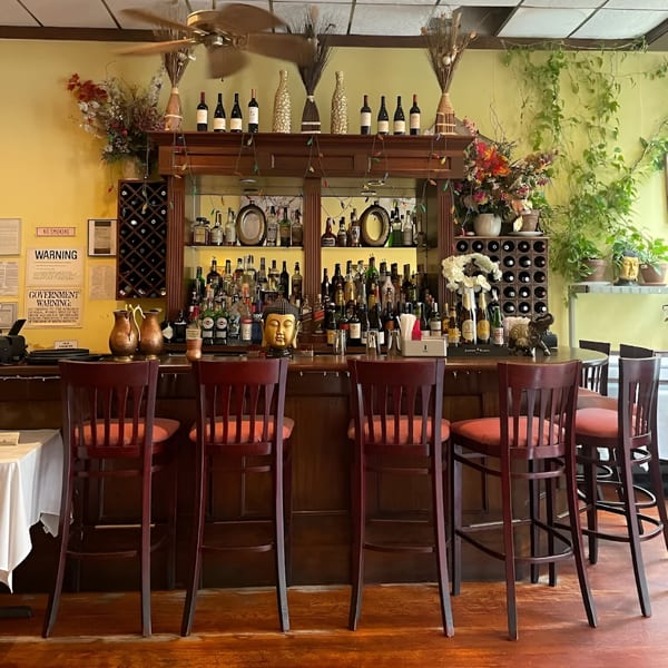 A cozy Indian restaurant bar with a golden Buddha head, bottles, and wooden stools.