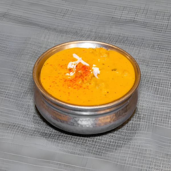 A golden Indian curry in a hammered metal bowl, garnished with white cream and red spice.