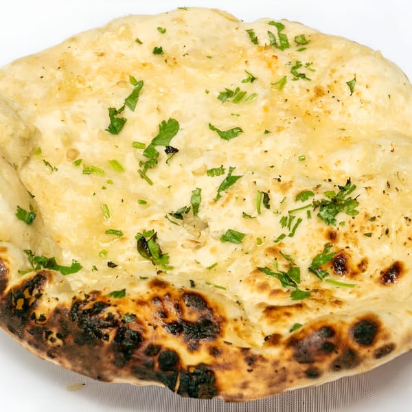Close-up of a golden-brown naan bread, garnished with fresh green cilantro, from Manhattan Valley Indian Restaurant.