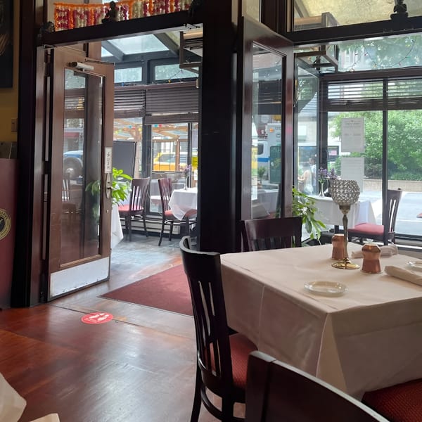 Interior view of Manhattan Valley Indian Restaurant with tables, chairs, and large windows looking out to the street.