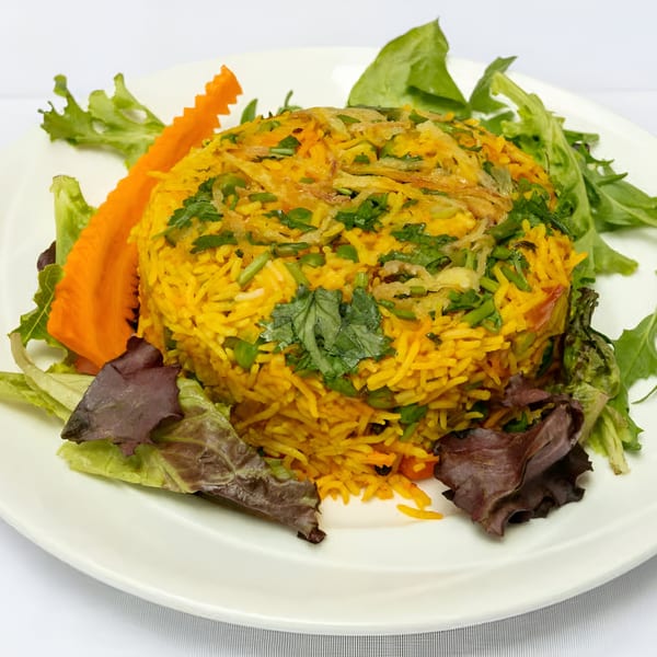 Indian biryani rice with peas, cilantro, and fried onions, garnished with lettuce and carved carrot.