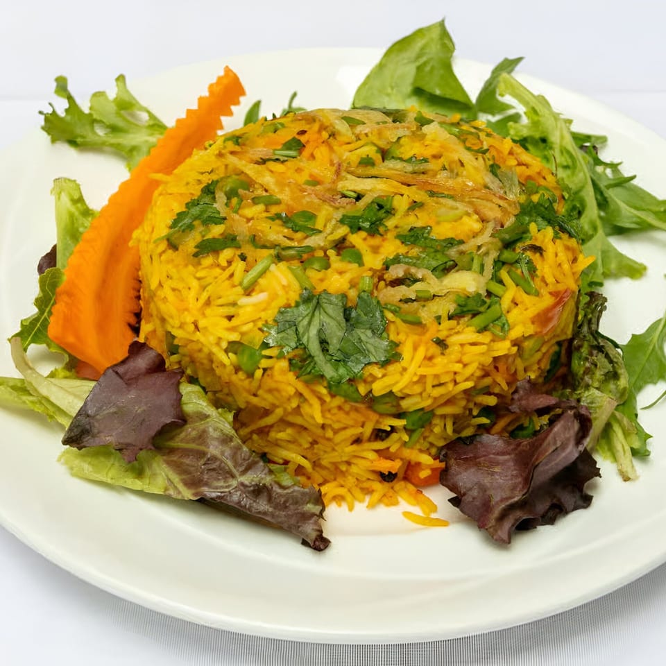 Indian biryani rice with peas, cilantro, and fried onions, garnished with lettuce and carved carrot.