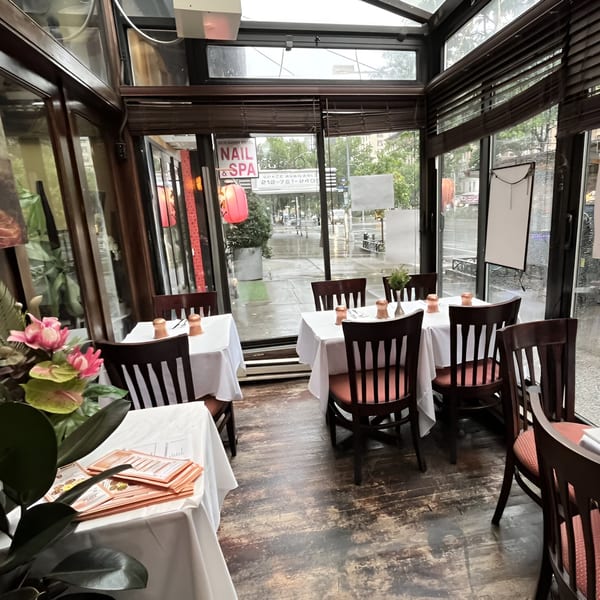Interior of Manhattan Valley Indian Restaurant with tables set by large windows overlooking a rainy street.